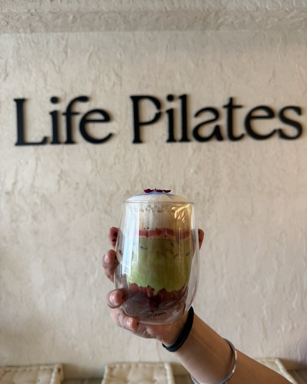 A layered matcha held up against the Life Pilates wall