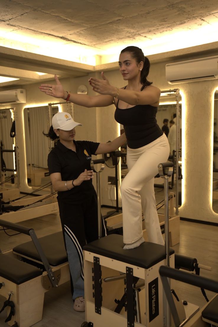 An instructor guiding a member through standing work on the reformer