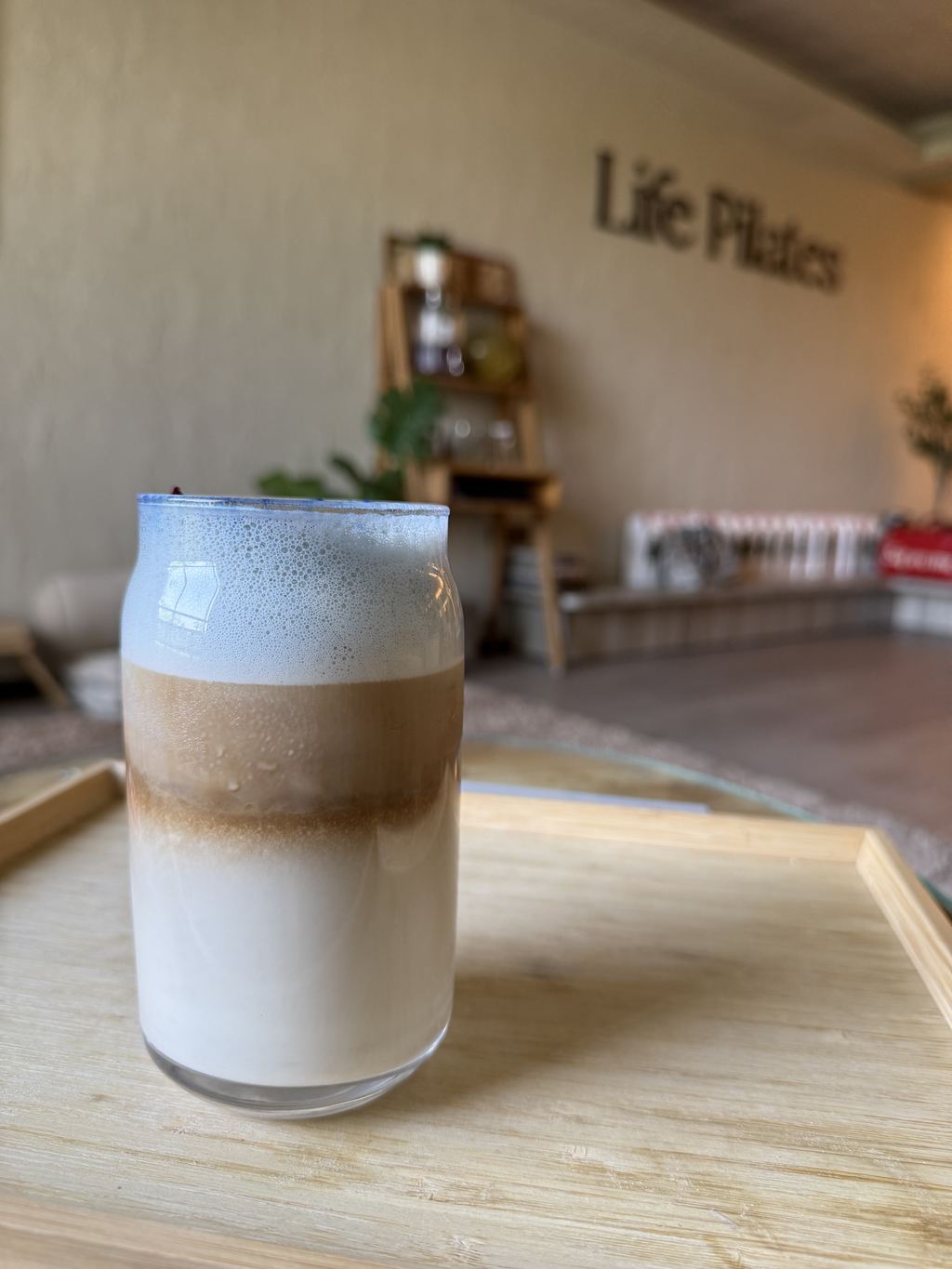 A layered iced latte on a wooden tray in front of the Life Pilates wall lettering